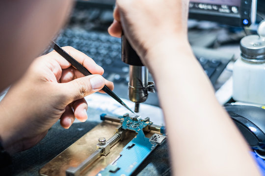 Close-up Of Technician's Hand Showing Process Of Repair And Fix Cell Phon With Soldering Iron.