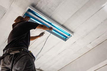 Technician is installing fluorescent bulbs on ceiling of building. Home improvement concept.