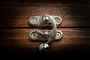 An elegant metal sliding clasp lock screwed into the lid of a wooden box.