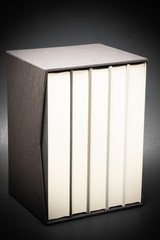 A set of five monochromatic cloth-bound books stored inside a black hard cardboard slipcase set on a slightly graduated and subtly textured dark background.