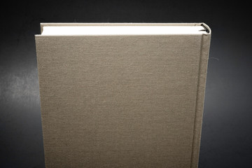 A close-up look at the top portion of a single cloth-bound book with black ribbon bookmarker and set on a slightly textured and gradient dark background.