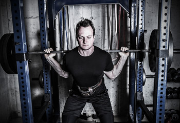 Fototapeta na wymiar Young man weight training in a gritty basement gym.