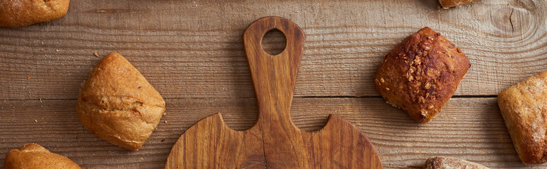 top view of fresh homemade buns near wooden chopping board on rustic table, panoramic shot