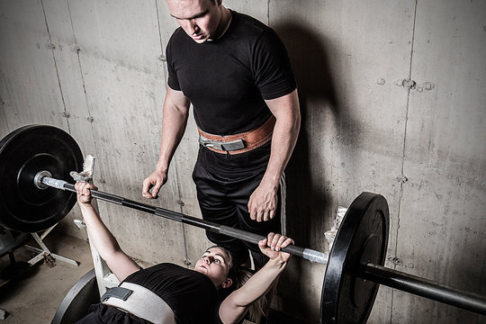 Young man and woman powerlifting in a gritty basement gym.