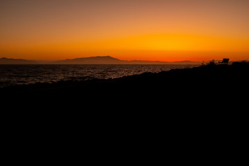 A quiet empty bench silhouette over looking the ocean during a warm sunset at the Berkeley marina.