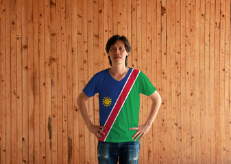 Man wearing Namibia flag color shirt and standing with akimbo on the wooden wall background.