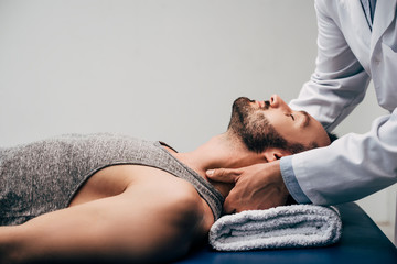 chiropractor massaging neck of handsome man lying on Massage Table on grey - obrazy, fototapety, plakaty