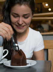 Woman eats chocolate cake and drinks coffee in cafe. Lifestile photo with a girl in white