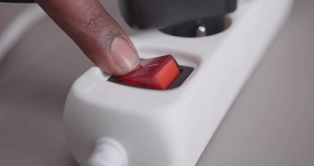 Black man turns on and off the power switch of a power distributing unit in order to save energy costs.