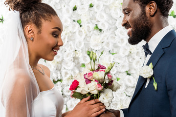 surprised african american bride looking at flowers near bridegroom