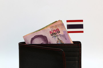 Five hundreds of banknote Thai baht and mini Thailand nation flag stick on the black wallet with white background.