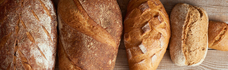top view of fresh homemade loaves of bread and bun on wooden rustic table, panoramic shot