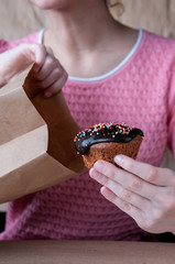 Girl in a pink blouse pulls out of a paper bag muffin with chocolate icing