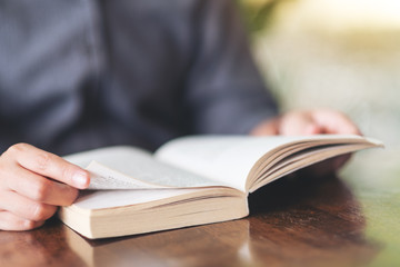 Closeup image of a woman holding and reading a vintage novel book on wooden table