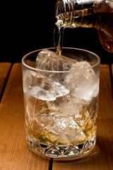 茶色い木目背景でロックグラスにウィスキーを注ぐ
