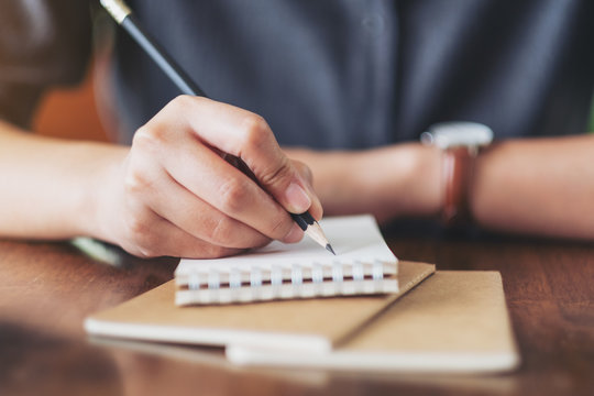Closeup image of a woman's hand writing on blank notebook on wooden table