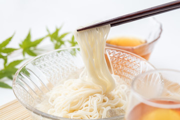 白背景でガラスのお皿に入ったそうめんを箸で食べる