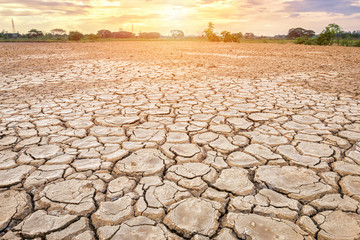 Brown dry soil or cracked ground texture on blue sky background with white clouds sunset.