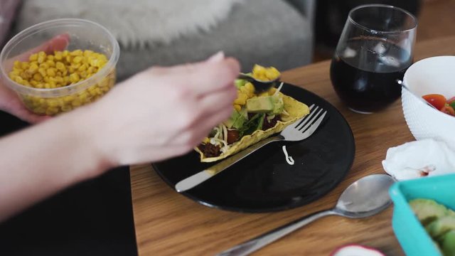 Putting some corn on vegan minced soy meat laying on a hard shell tortilla. Showing extra ingredients in the background.
