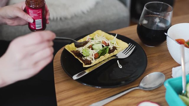 Putting some chipottle paste on vegan minced soy meat laying on a hard shell tortilla. Showing extra ingredients in the background.