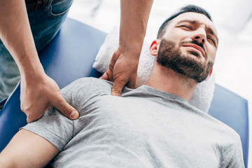 chiropractor massaging shoulder of man lying on Massage Table in hospital