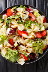 Organic pasta farfalle salad with avocado, strawberries, lettuce, dressed with balsamic sauce close-up. Vertical top view