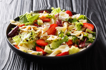 Healthy salad of farfalle pasta with avocado, strawberries, fresh lettuce and balsamic sauce close-up on a plate. horizontal