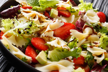 Farfalle pasta with avocado, strawberries, mix lettuce and balsamic dressing close-up on a plate. horizontal