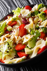 Summer pasta salad with avocado, strawberries, lettuce, dressed with balsamic sauce close-up on a plate. vertical