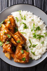 Delicious stewed ribs in a spicy sauce served with white rice close-up on a plate. Vertical top view