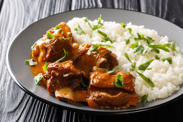 Beef ribs in a spicy sauce with rice garnish close-up on a plate. horizontal