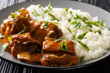 Delicious stewed ribs in a spicy sauce served with white rice close-up on a plate. horizontal