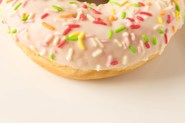 Fresh glazed donut with colorful sprinkles on a white plate.