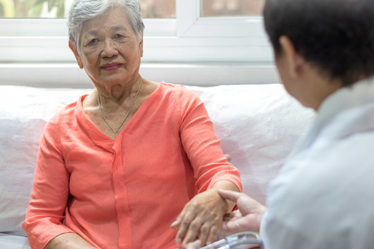 Parkinson and Alzheimer female senior elderly patient with caregiver in hospice care. Doctor hand with stethoscope check up older woman people. Old aging person seeing medical physician in hospital.