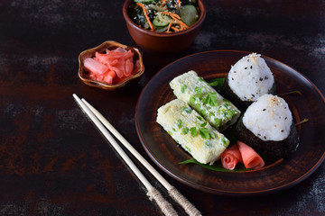 Mix of Japanese food - rice balls onigiri, omelette, pickled ginger, sunomono wakame cucumber salad and chopsticks. Asian breakfast or lunch background