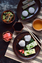 Mix of Japanese food - rice balls onigiri, omelette, ginger, sunomono wakame cucumber salad. Traditional dessert of bean and green tea matcha - jelly yokan, daifuku mochi. Asian breakfast or lunch