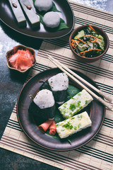 Mix of Japanese food - rice balls onigiri, omelette, ginger, sunomono wakame cucumber salad. Traditional dessert of bean and green tea matcha - jelly yokan, daifuku mochi. Asian breakfast or lunch