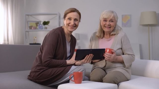 Elderly women smiling, watching entertainment show on tablet, fast internet