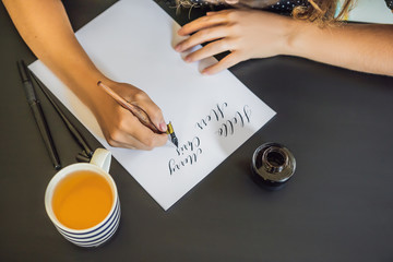 Calligrapher Young Woman writes phrase on white paper. Inscribing ornamental decorated letters....