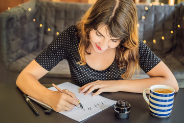 Calligrapher Young Woman writes phrase on white paper. Inscribing ornamental decorated letters....