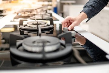 Male hand turning switch knob on modern gas stove in kitchen showroom. Cooking appliance in domestic kitchen. Home improvement and House interior design concepts