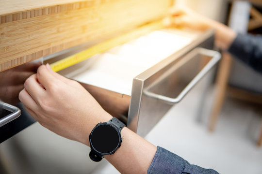 Asian man interior designer using tape measure for measuring size of stainless steel drawer on modern counter in kitchen showroom in furniture store. Shopping material design for home improvement. - Powered by Adobe