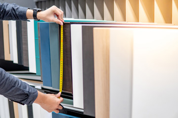 Male hand using tape measure on cabinet panel choosing materials or countertops for built-in...