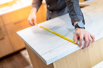 Male hand designer using tape measure for measuring white granite countertops on modern kitchen...