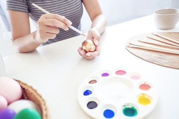 Woman painting easter eggs with white table.