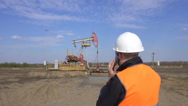 Male Chief Inspector In A Signal Vest Talking On The Phone On The Background Of A Pumping Station Oil, Gas And Combustible Fuel Industry, Pumpjack, Engineering