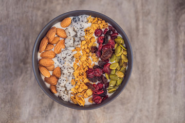 Mango smoothies bowl with almond, dragon fruit, dried cherries, pumpkin seeds and granola on wooden background