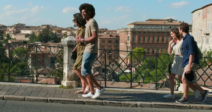Four happy tourist people walking amazed through street visiting Perugia medieval city.Side follow.Friends italian vacation trip in Umbria.4k slow motion