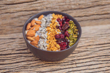 Mango smoothies bowl with almond, dragon fruit, dried cherries, pumpkin seeds and granola on wooden background