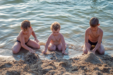 three boys build sand castles on the beach in summer while swimming